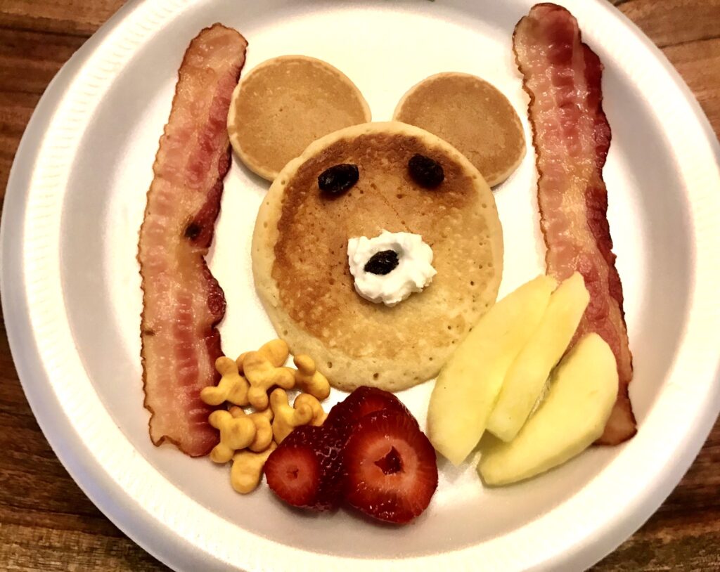 Pancakes made into a bear face with raisins for the eyes and whipped cream for the nose and pancake ears. 