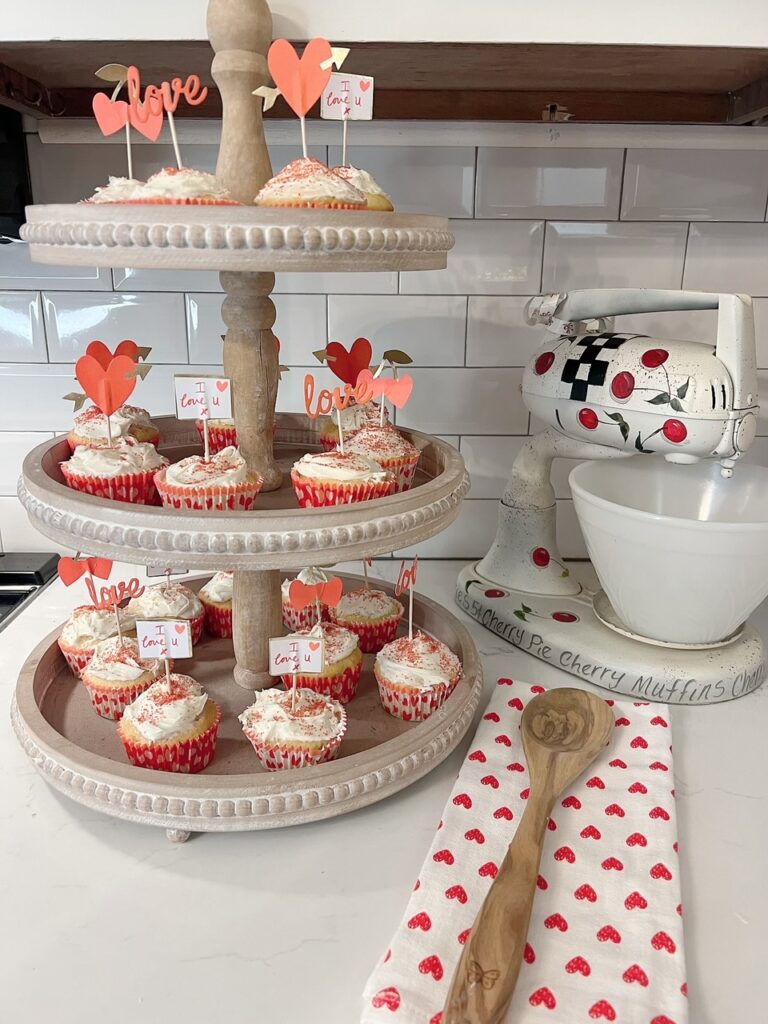 Valentine Cupcakes on 3 tier tray with vintage mixer and heart tea towel with wooden spoon