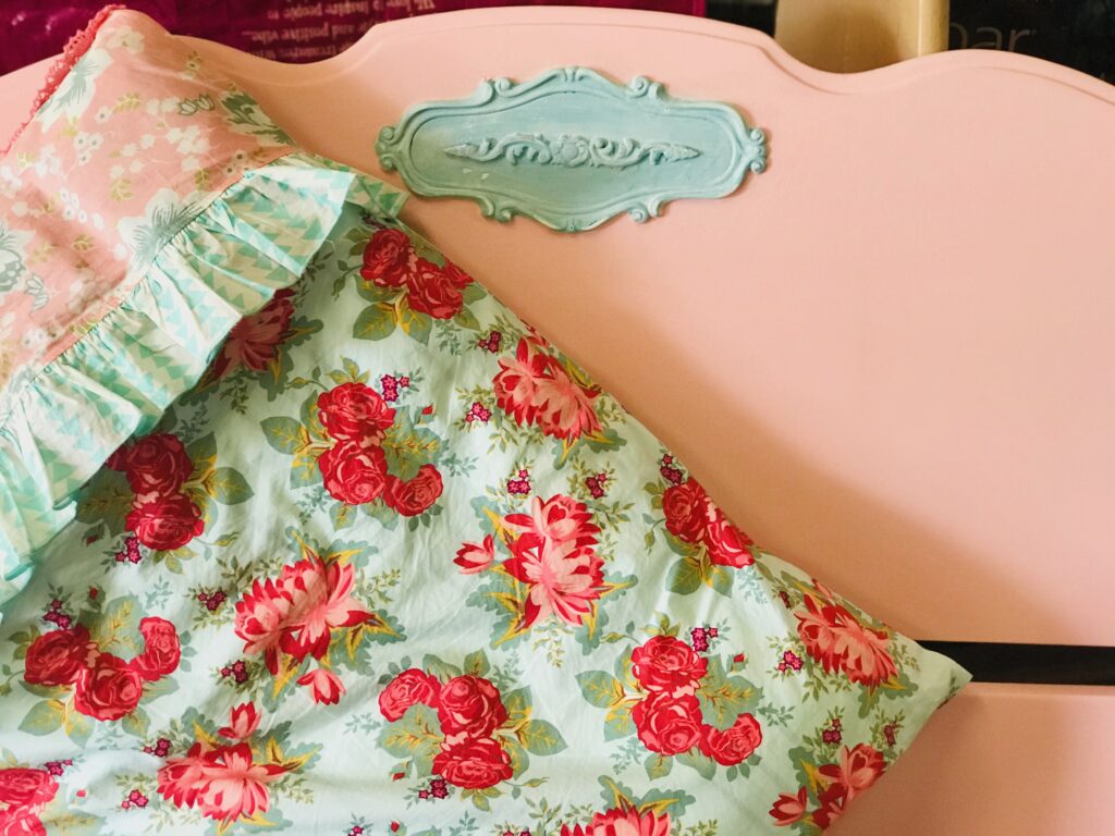 Pink painted headboard with aqua detail, with aqua pillow sham with pink flowers. 
